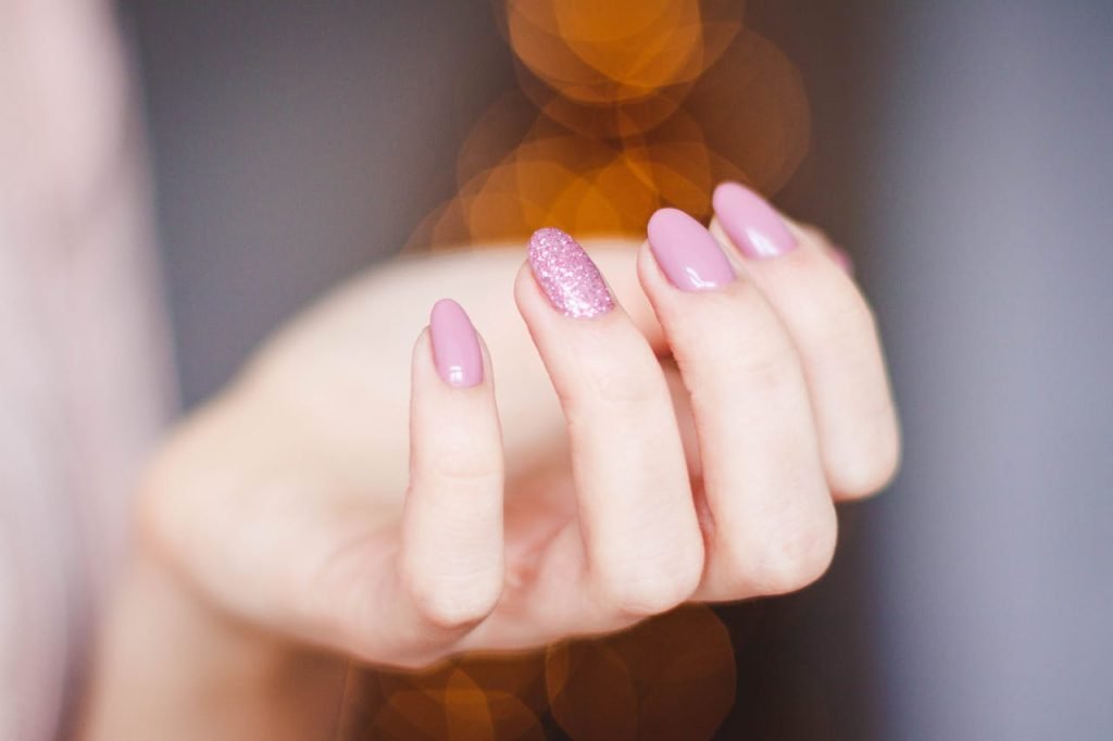 A close-up of a womans hand displaying a stylish pink glitter manicure, highlighting nail art details.